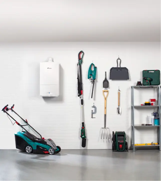 A neatly organized garage with a lawnmower, various gardening tools hanging on the wall, a shelf with storage boxes and supplies, and a white gas boiler mounted on the wall.