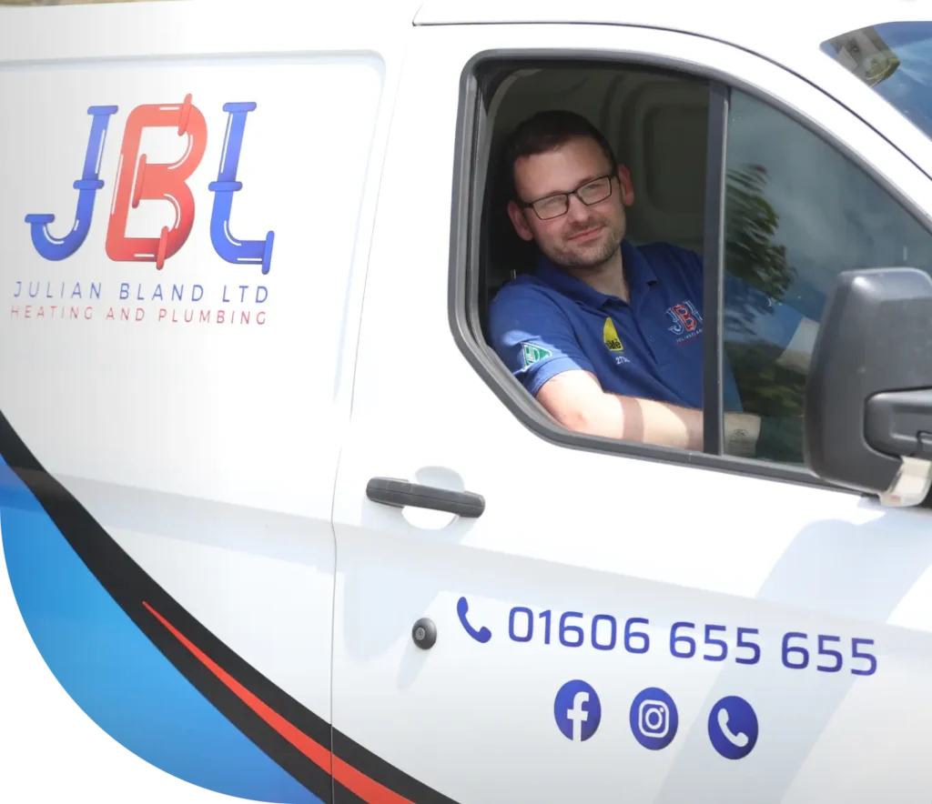 A JBL technician wearing a glasses and a blue shirt is sitting in the driver's seat of a white van with "Julian Bland Ltd Heating and Plumbing" and contact details on it, ready to bring reliable home services right to your doorstep.